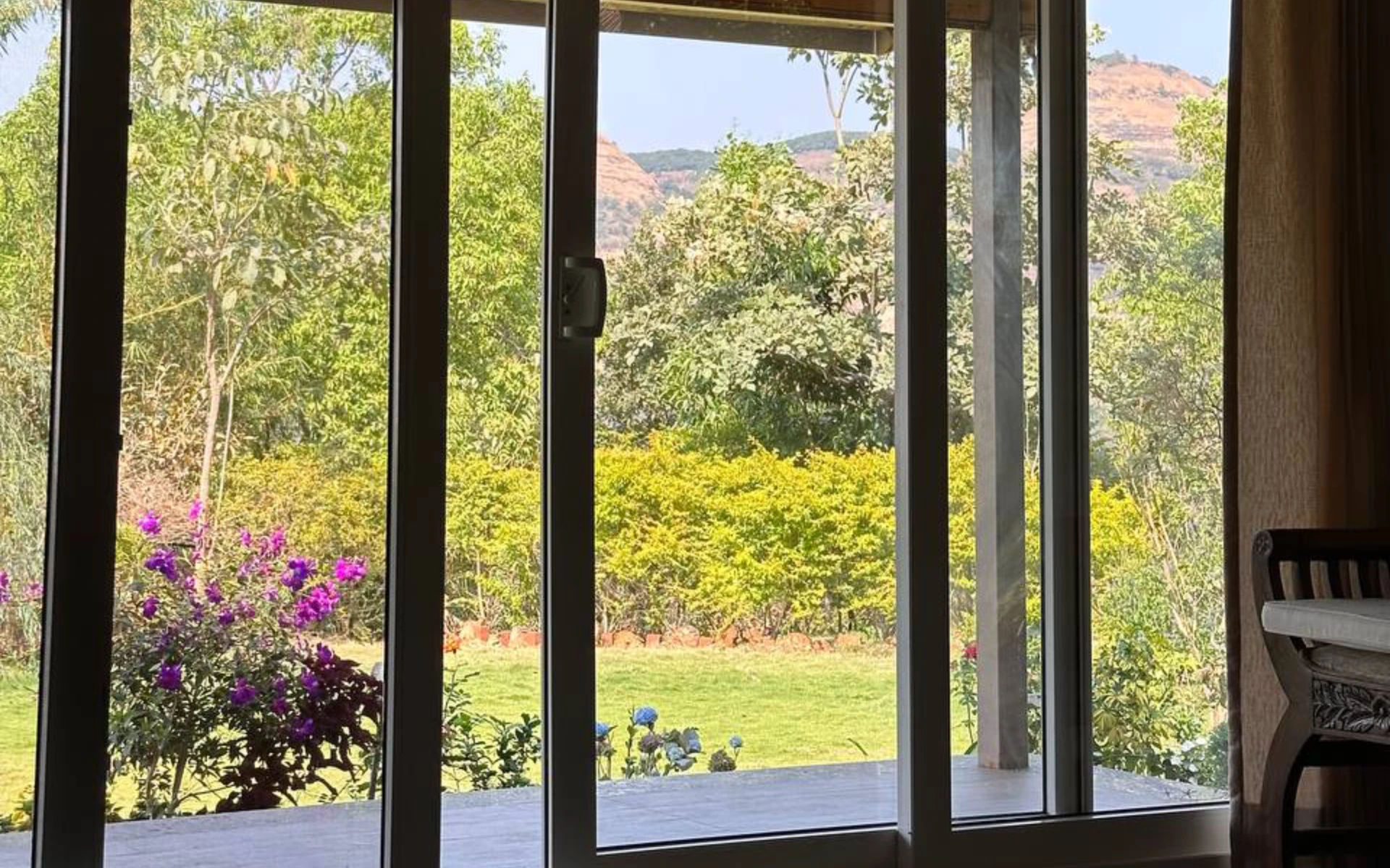 Morning light through glass doors at Moonstone Cottage — garden, bougainvillea and Sahyadri mountains, Kamshet